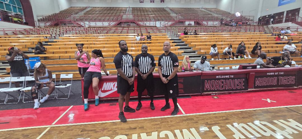 Three referees in black-and-white stripes stand at center court at Forbes Arena — Welcome to Morehouse, Home of the Maroon Tigers signage visible