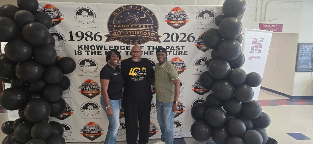 Three AMB attendees — woman, elder, and young man — pose in front of the 40th Anniversary 1986–2026 step-and-repeat at Morehouse College